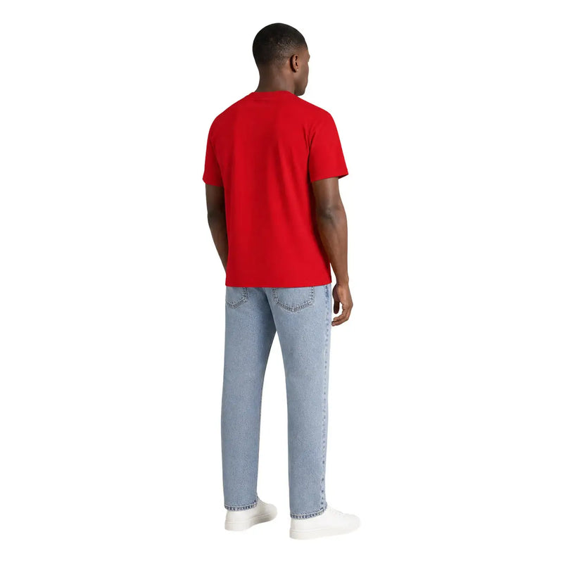 Un homme porte un t-shirt rouge à manches courtes en coton bio Tommy Hilfiger avec un jean délavé.