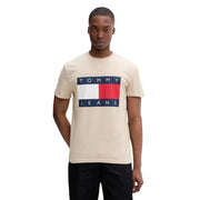 T-shirt beige Tommy Hilfiger pour homme en coton bio, orné du logo drapeau rouge, blanc et bleu marine et de l'inscription « Tommy Jeans ».