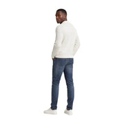 Un homme portant un jean slim bleu en coton Tommy Hilfiger Scanton pour homme, associé à un pull en maille à manches longues couleur crème.