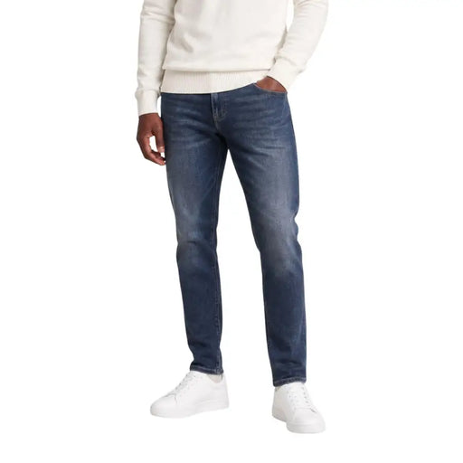Jean slim bleu marine Tommy Hilfiger Scanton pour homme, en coton, délavage foncé et subtilement délavé, porté par un mannequin en tenue décontractée.