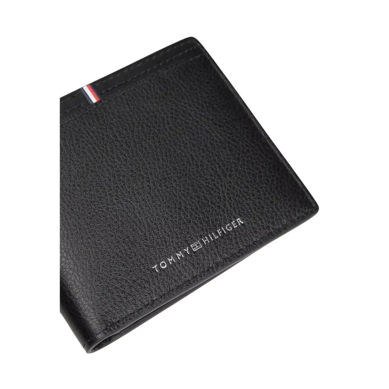 Tommy Hilfiger Portefeuille homme en cuir noir texturé avec logo argenté et languette à rayures rouges, blanches et bleues visible sur le devant