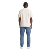 Un homme portant un vêtement couleur crème Tommy Hilfiger T-shirt à manches courtes en coton bio blanc pour homme, à porter avec un jean bleu