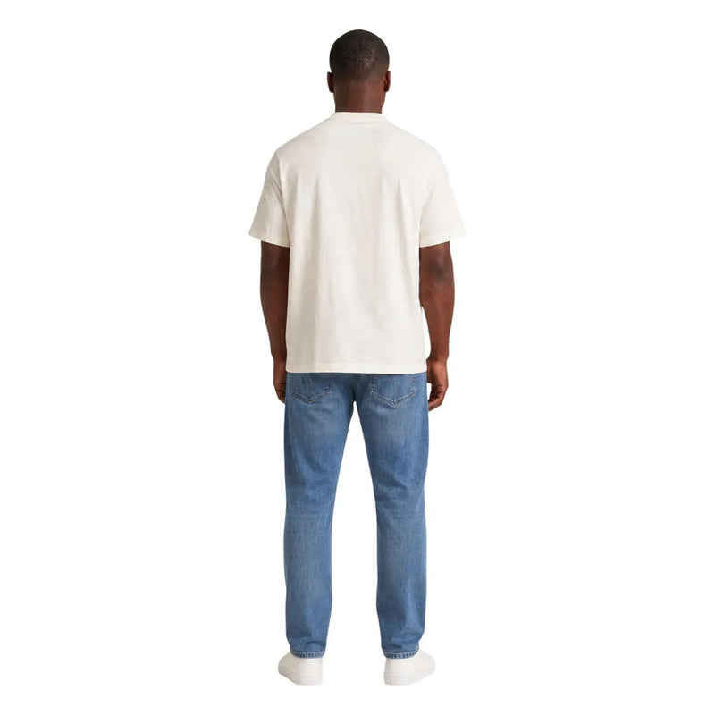 Un homme portant un vêtement couleur crème Tommy Hilfiger T-shirt à manches courtes en coton bio blanc pour homme, à porter avec un jean bleu