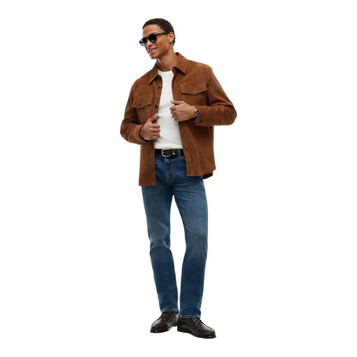 Jean slim Tommy Hilfiger bleu pour homme, porté par le mannequin avec une veste en daim marron, poches poitrine et col visibles (vue de face).