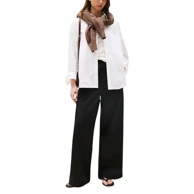 A woman wearing Tommy Hilfiger women black organic cotton wide-leg trousers with a white shirt and brown knitted scarf