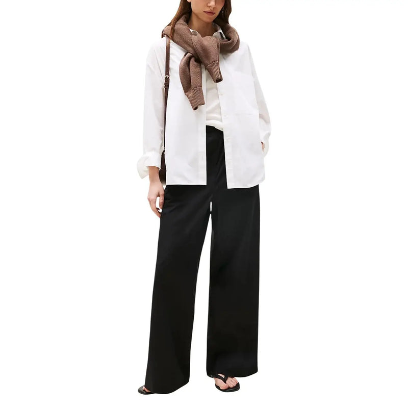 A woman wearing Tommy Hilfiger women black organic cotton wide-leg trousers with a white shirt and brown knitted scarf