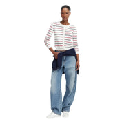 Une femme porte un cardigan blanc à manches longues Tommy Hilfiger en maille de coton biologique à rayures rouges et noires.
