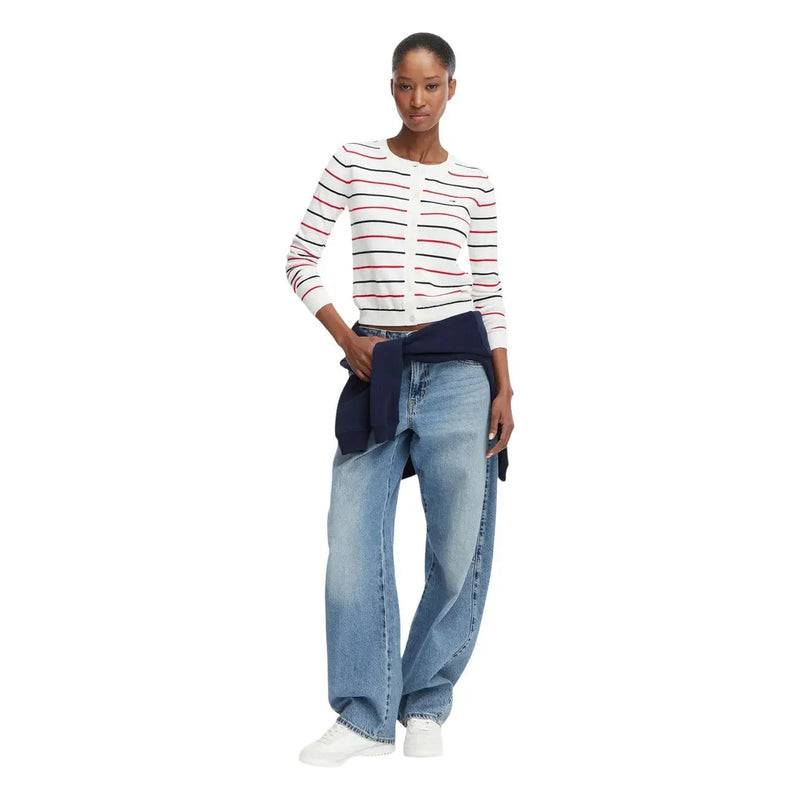 Une femme porte un cardigan blanc à manches longues Tommy Hilfiger en maille de coton biologique à rayures rouges et noires.