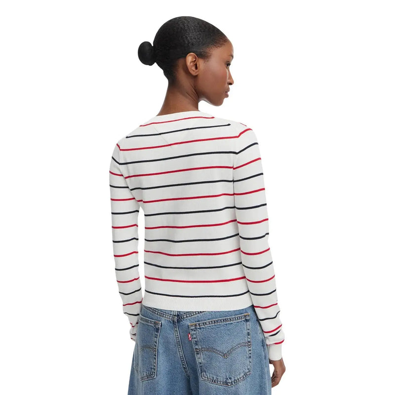 Une femme porte un pull Tommy Hilfiger pour femme, blanc, en maille de coton biologique, à manches longues et col rond, orné de rayures.