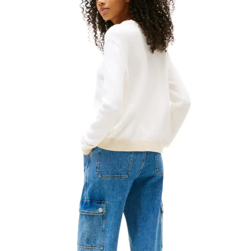Woman wearing a white long-sleeved top and blue cargo jeans for Tommy Hilfiger product display