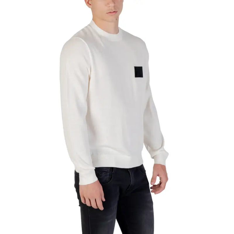 White long sleeved crewneck sweater made of soft fabric featuring a black square patch on the left chest