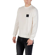 White long sleeved crewneck sweater in cream color with a black square patch on the left chest