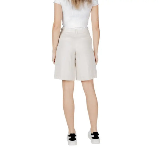 Woman wearing beige Bermuda shorts and white sneakers in a casual fashion setting