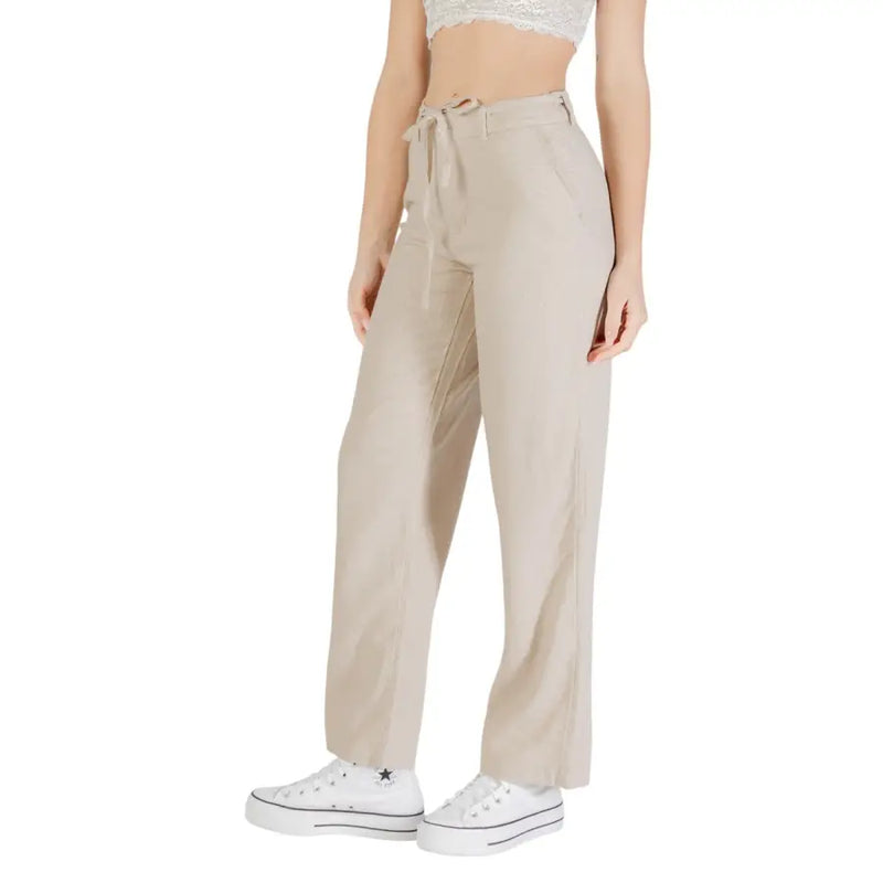 Woman wearing beige linen viscose trousers with front pockets and white platform sneakers