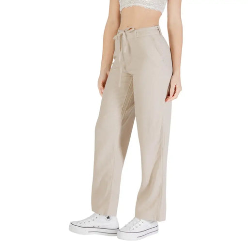 Woman wearing beige linen viscose trousers with front pockets and white platform sneakers