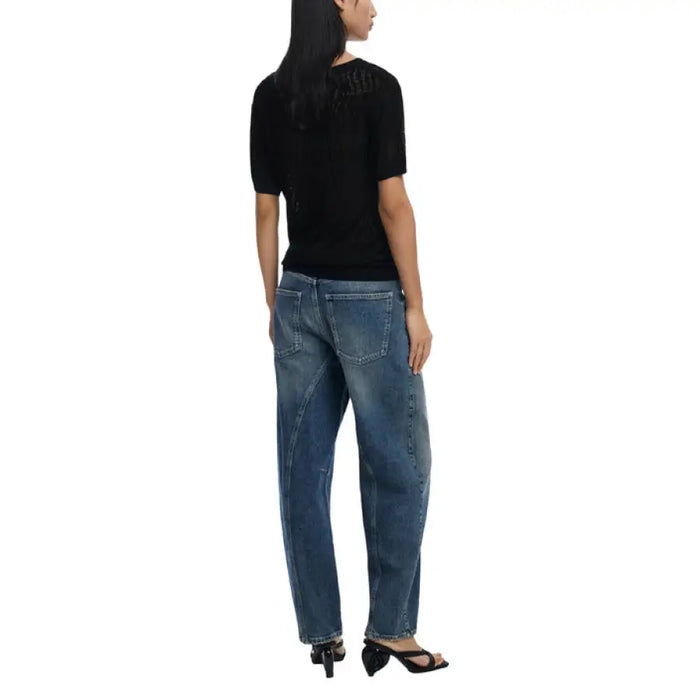Woman wearing a black knit top with leaf pattern and blue jeans