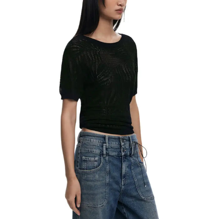 Woman wearing a black knit top with leaf pattern and blue jeans in product display