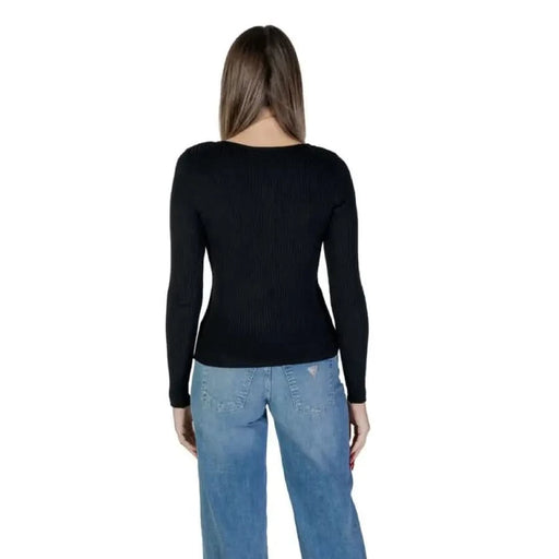 Woman in a black ribbed long-sleeve shirt and blue jeans showcasing Vila Clothes sweater