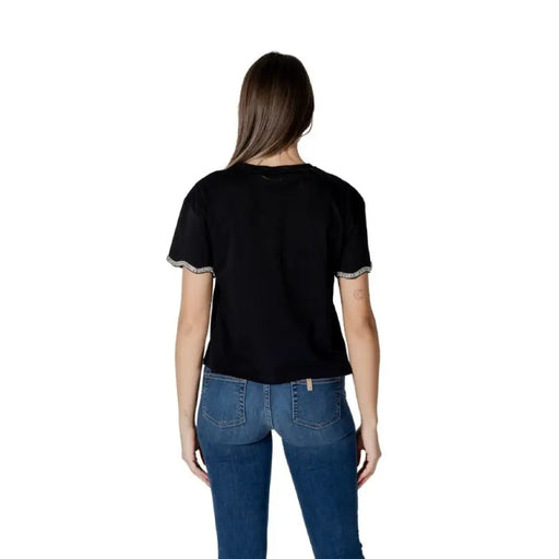 Woman wearing a black t-shirt with embellished sleeves and blue jeans
