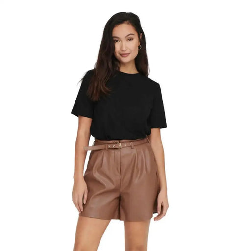 Femme vêtue de noir t-shirt et un short en similicuir marron affichant un look décontracté et élégant