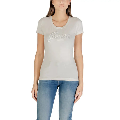 Femme portant un pantalon ajusté de couleur claire Guess T-shirt avec imprimé strass et jean bleu