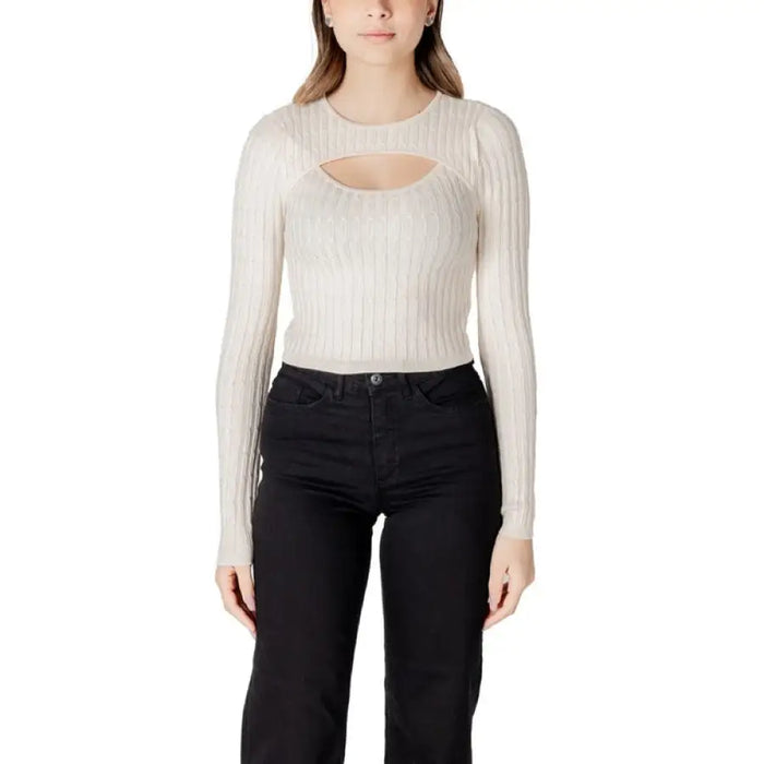Woman wearing a long-sleeved beige ribbed knit sweater with a chest cutout and black pants