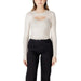 Woman wearing a long-sleeved beige ribbed knit sweater with a chest cutout and black pants