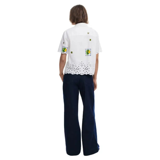 Woman wearing a white embroidered short sleeved shirt with dark blue pants