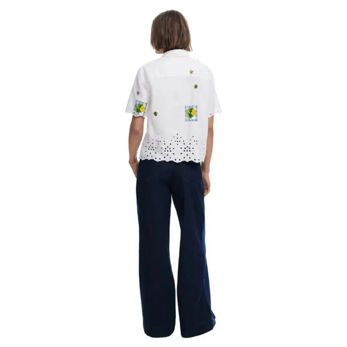 Woman wearing a white embroidered short sleeved shirt with dark blue pants