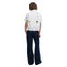 Woman wearing a white embroidered short sleeved shirt with dark blue pants