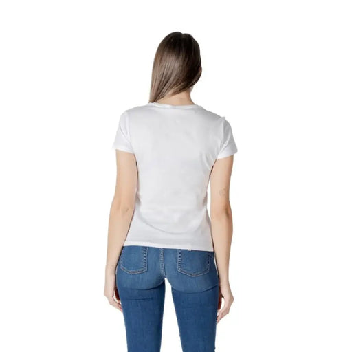 Woman wearing a white T-shirt with Tokyo graphic and blue jeans in front of a plain background
