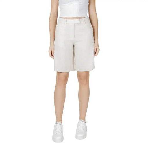 Woman wearing beige Bermuda shorts paired with white sneakers in a stylish casual outfit