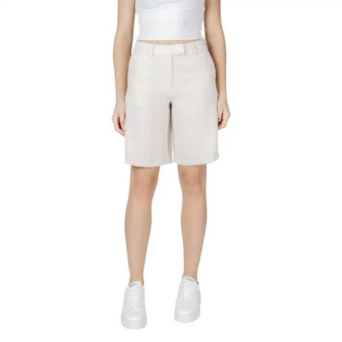 Woman wearing beige Bermuda shorts paired with white sneakers in a stylish casual outfit