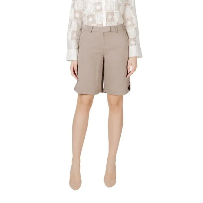 Woman wearing beige Bermuda shorts and white sneakers ensemble for casual wear