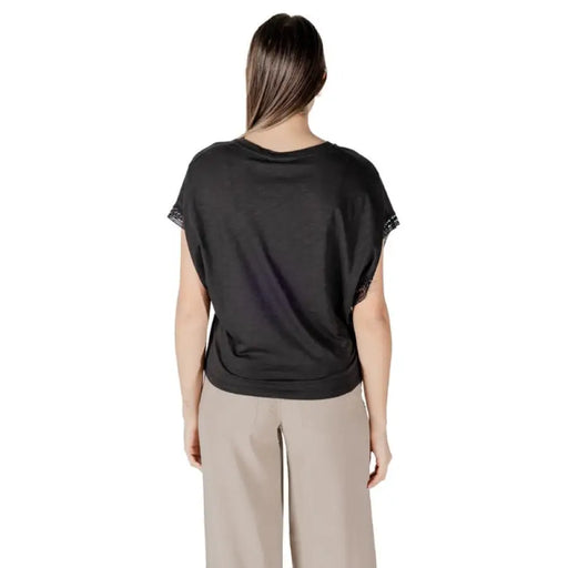 Woman wearing black V neck top with lace sleeves and beige pants in a fashion setting