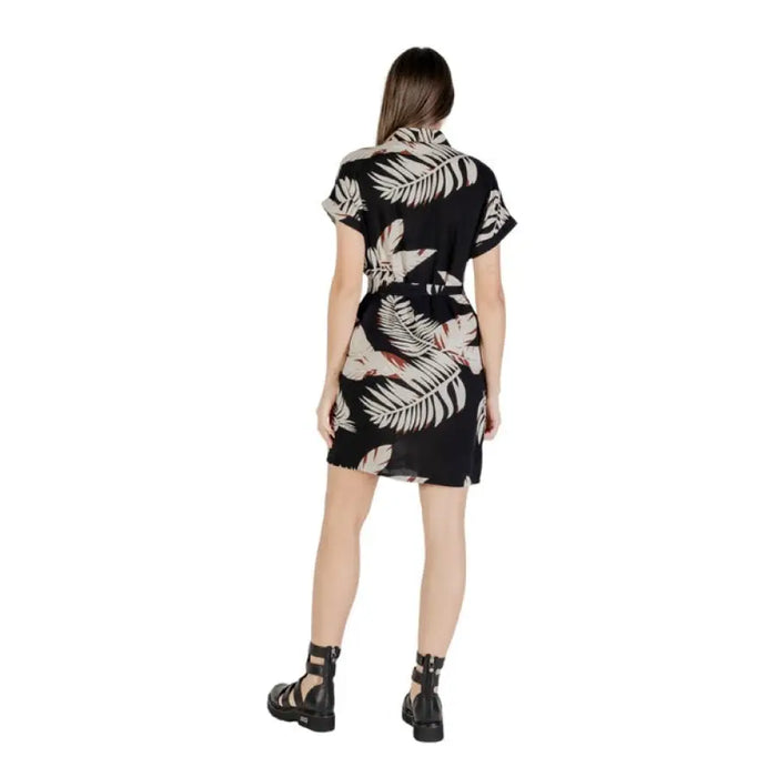 Woman wearing a black leaf-patterned romper and shirt dress in a product display