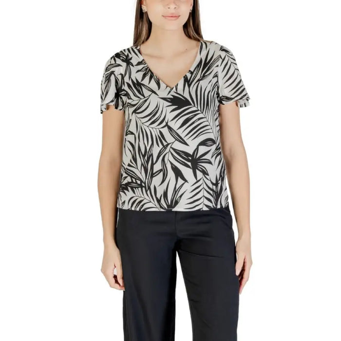 Woman wearing black and white leaf-patterned V-neck top with green shorts