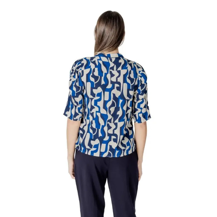 Woman’s blue and white patterned blouse paired with dark pants in product image