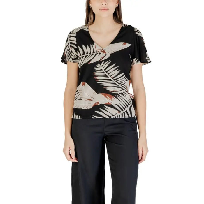 Woman wearing a leaf-patterned top and black pants from Womens Black V Neck Flutter Sleeve Top and Green Shorts collection