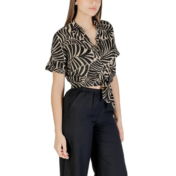 Woman wearing leaf-patterned tie-front blouse and black pants for women product display