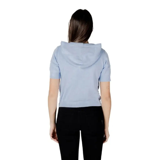 Woman wearing light blue hooded short-sleeve cardigan and black pants displayed