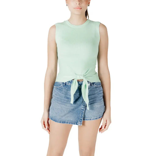 Woman wearing mint green tie-front tank top and denim mini skirt showcasing style