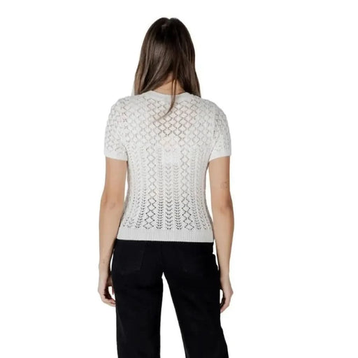 Woman wearing a white round neck open-knit short-sleeved sweater in a stylish setting