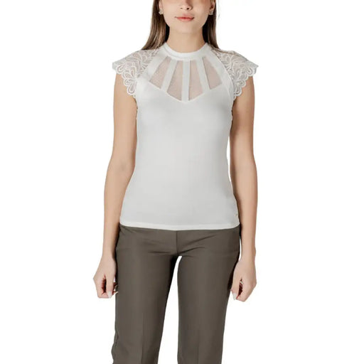 Woman wearing a white lace-trimmed top with gray pants, featuring a black lace trimmed sleeveless top