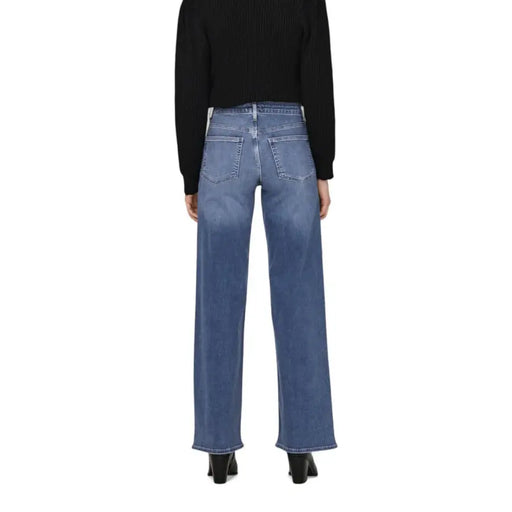 Woman wearing black long-sleeved ribbed knit top and blue wide-leg jeans with pockets