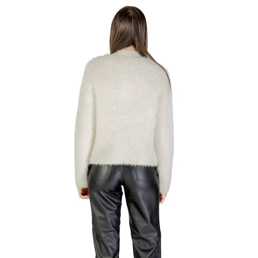Cream-colored fuzzy knit sweater with long sleeves and round neck paired with black faux leather trousers