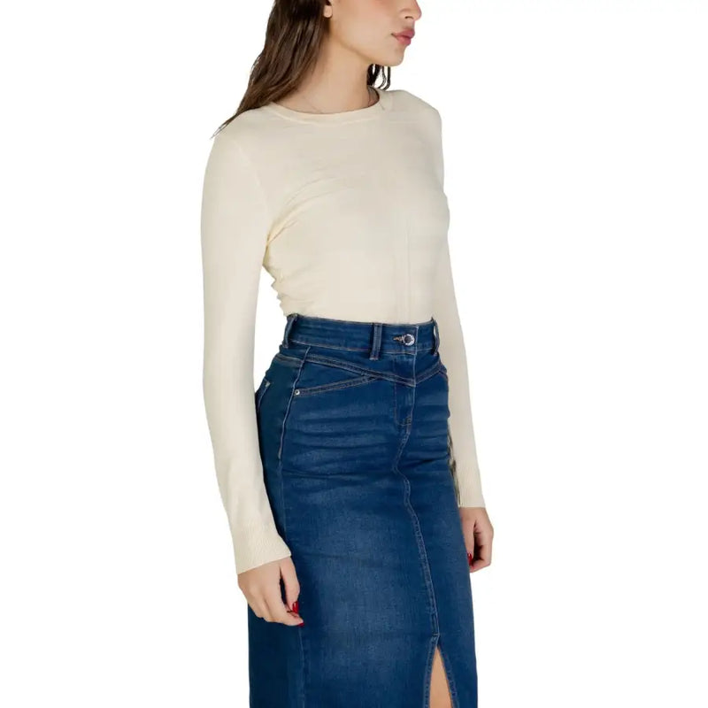 A woman wears a cream-colored long sleeve round neck viscose knit top paired with a dark blue denim skirt